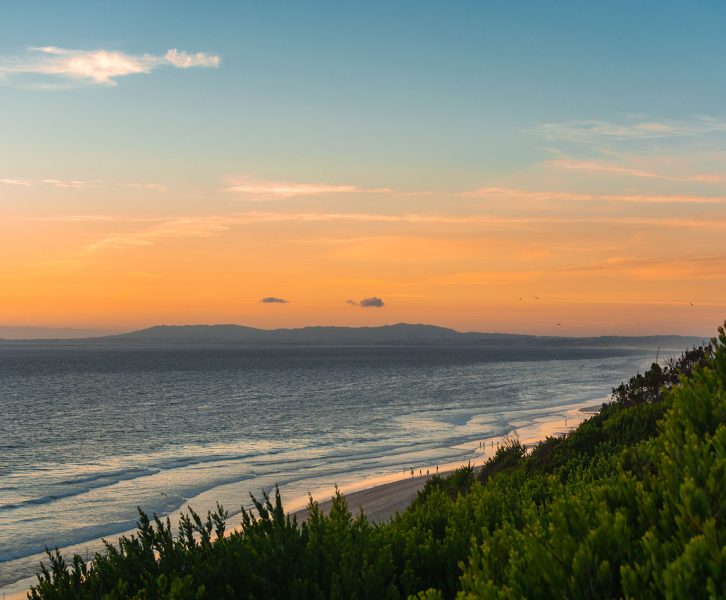 Praia da Adiça: Green vegetation, a calm sea, and an orange sunset over the Atlantic ocean